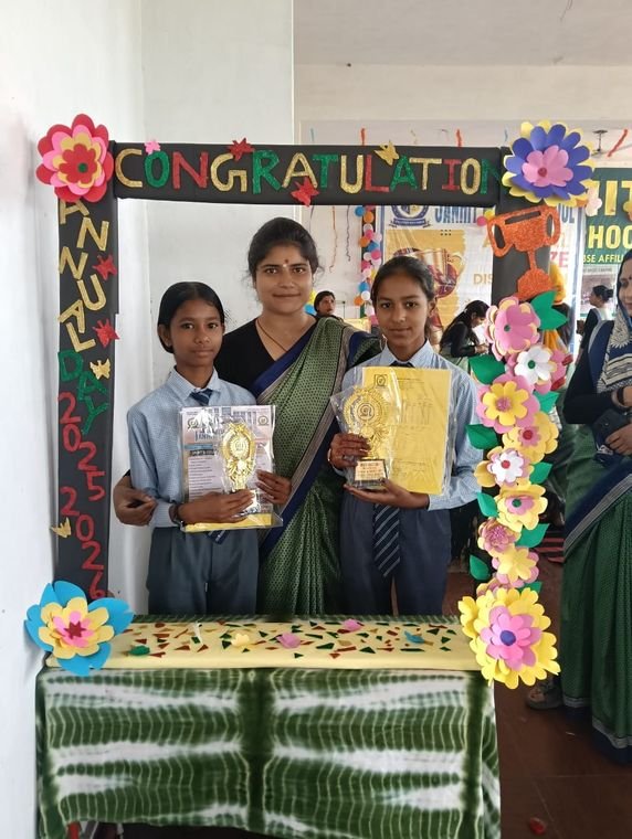 Two students holding trophies with their teacher at Janhit World School